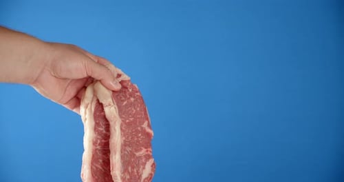 A Man's Hand Holds a Striploin Steak Raw.