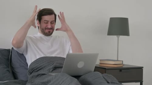 Man Using Laptop in Bed, Frustrated