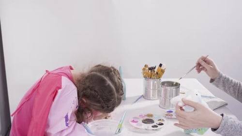 Little girl painting paper mache figurines with acrylic paint for her homeschooling art project.
