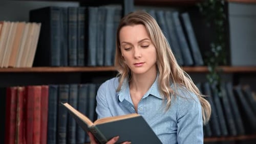 Confident Blonde Woman Reading Interesting Paper Book Turning Pages at Library Bookshelves Cupboard