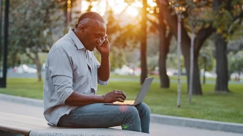 Adult Using Laptop and Phone on Park Bench