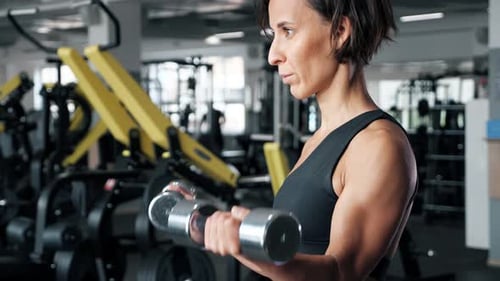 Une femme mature sportive fait des exercices de biceps avec des haltères dans la salle de sport