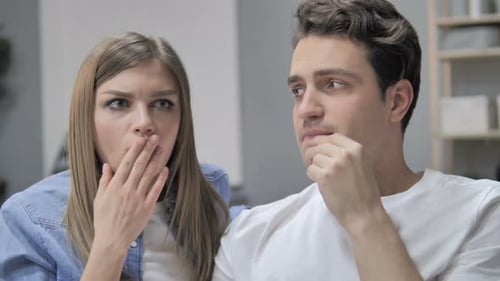 Schockiertes junges Paar auf der Couch wundert sich