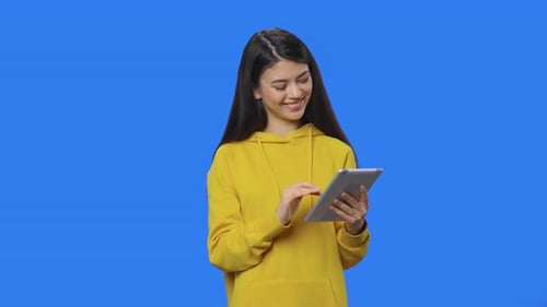 Young Woman Using Tablet Against Blue Backdrop