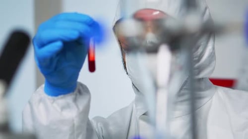 Nahaufnahme eines Chemikers, der eine Blutprobe hält und einen Overall trägt