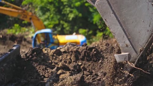 Bucket of tractor digs the ground. Excavator digging the soil on the background of green trees