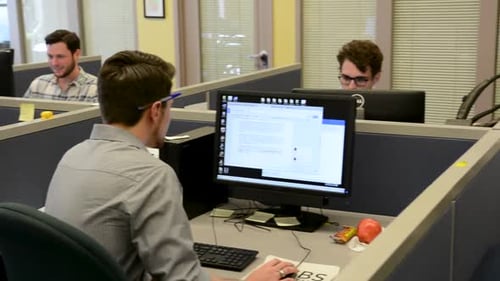 Linke Schwenkaufnahme junger Berufstätiger, die in Kabinen am Computer arbeiten