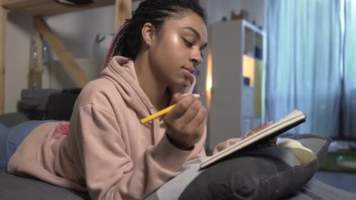 Woman Lies on Bed Writing in Notebook