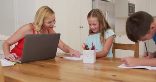 Woman Helping Children with Schoolwork at Dining Table