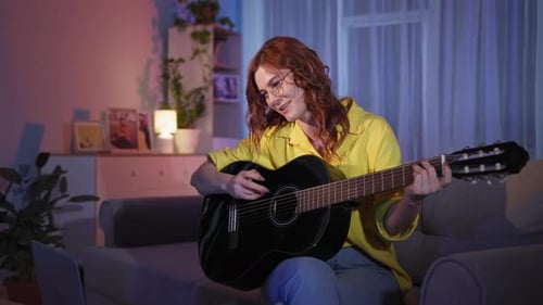 Woman Plays Guitar and Sings on Sofa at Night
