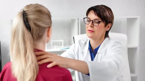 Mature Doctor Examines Patient's Neck in Office