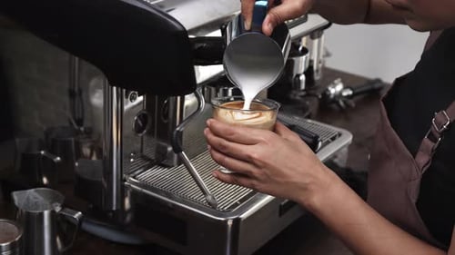 Barista travaillant dans un café, versant du lait cuit à la vapeur dans la tasse, préparant du café latte art au comptoir