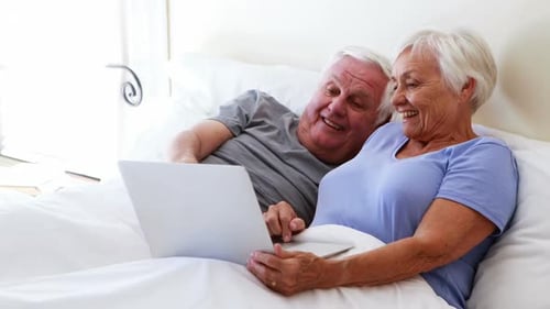 Smiling Elderly Couple Using Laptop in Bed