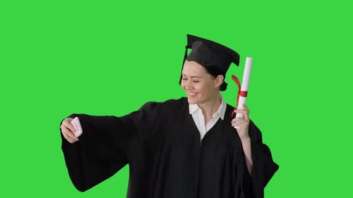 Happy Female Graduate Holding Diploma and Making Selfie on Her Phone on a Green Screen, Chroma Key.