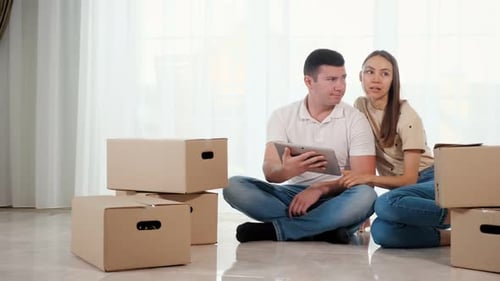 Couple Using Tablet Surrounded by Boxes in New Home