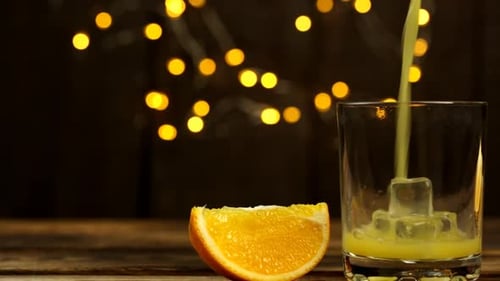 Pouring Beverage into Glass with Ice and Orange Slice