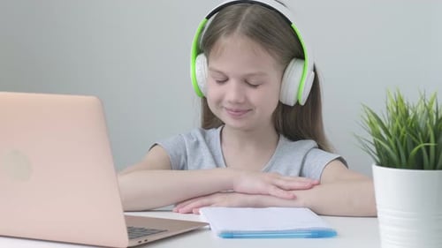 Happy School Girl Wearing Wireless Headphones Studying Online at Virtual Class with Teacher Tutor