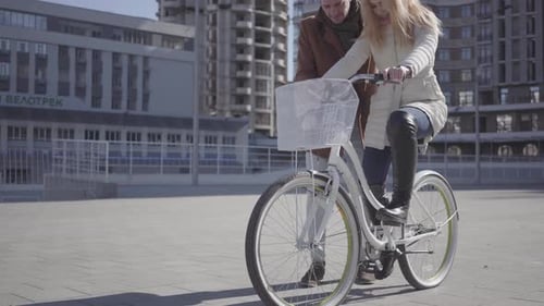 Handsome Man in Brown Coat Teaching His Girlfriend To Ride the Bicycle in the City, Both People