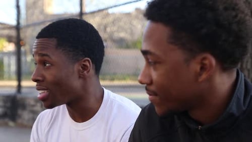 Zwei junge Basketballspieler unterhalten sich am Rande eines Straßenplatzes.