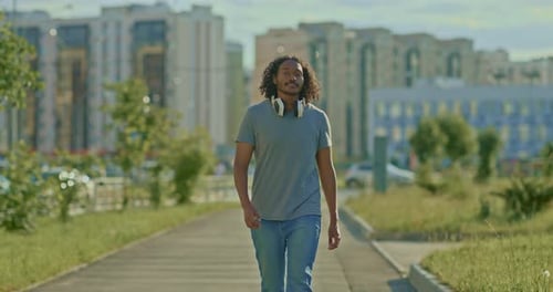 African American Guy Walks Through the Streets of the City in Headphones He is Happy