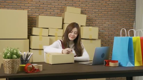 Woman Writes on Box Next to Laptop