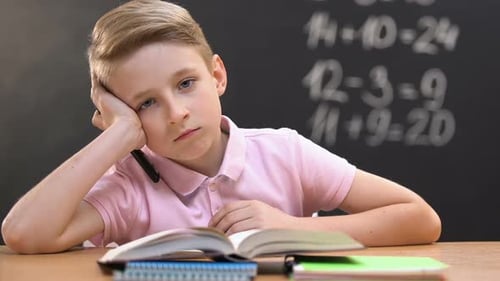 Bored Little Boy Sitting at School Desk During Math Lessons, Looking at Camera
