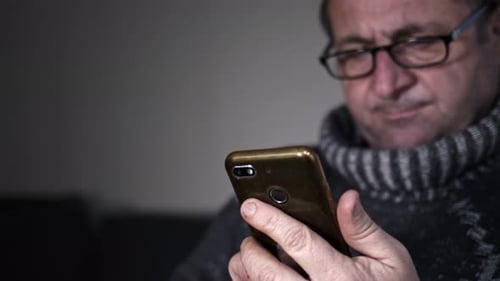 Senior Man Carefully Watches Video Playing On Mobile Phone