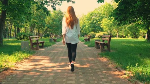 Rear Redheaded Girl Walks in Park Summer Season Daytime