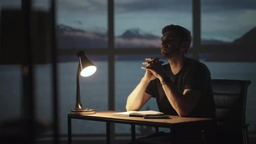 A silhueta de um homem pensativo sentado em uma mesa contra o fundo de uma janela com oceanos