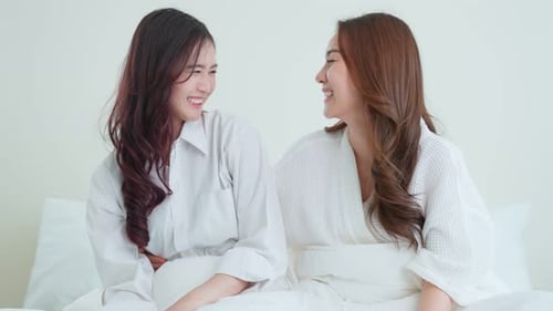 Two Young Women Smiling in White Bedroom