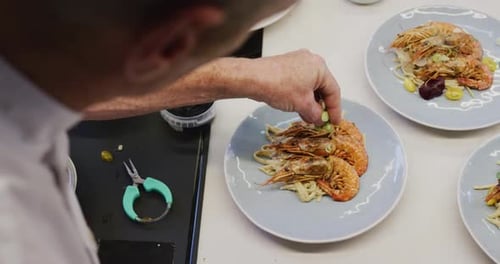 Caucasian male chef wearing chefs whites in a restaurant kitchen, putting food on a plate