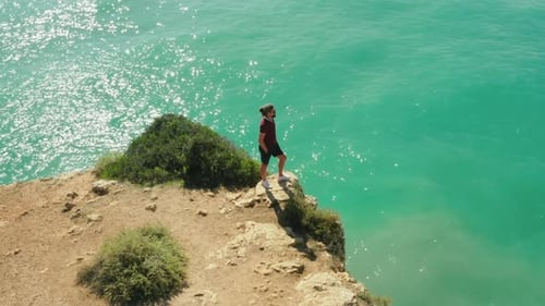 Breathtaking View of a Man Standing on a Rock with the Ocean Behind