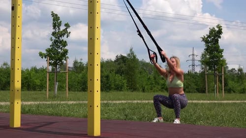 A Beautiful Fit Woman Does Assisted Squats with Jumps at an Outdoor Gym