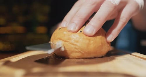 Mans Hands Cuts Burger Bun with Sesame Seeds Into Two Halves on Wooden Board Close Up. Slow Motion