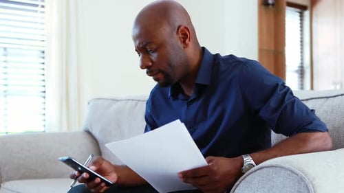 Man calculating invoices on mobile phone in living room 4k
