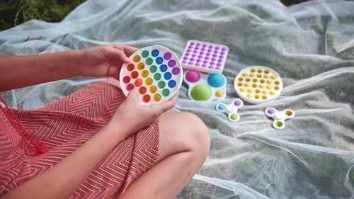 Teen Girl Plays with Antistress Toys Popit and Simple Dimple in the Park on a Summer Day