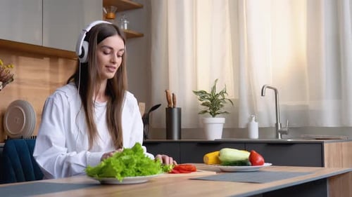 Woman with Headphones Chopping Vegetables in Kitchen