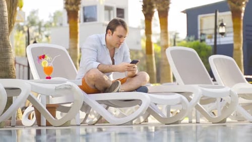 Man Relaxing Poolside Using Smartphone on Vacation