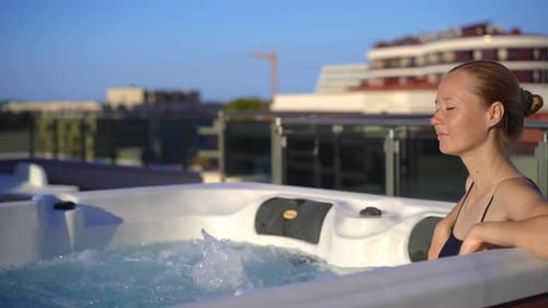 A Young Woman Relaxes in the Hot Tub on a Rooftop with a View on Mountains
