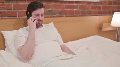 Man Lying in Bed Talking on Smartphone