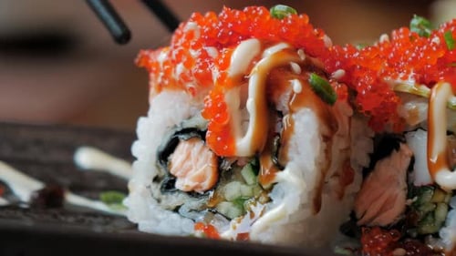 Close-up of Chopsticks Holds Sushi Roll Over a Plate in Restaraunt. Traditional Japanese Cuisine.