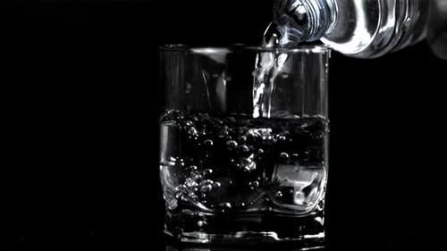 Pouring Clear Liquid into Glass on Black