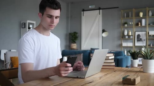 Man Uses Laptop and Smartphone at Home