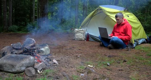 A Man Works on a Laptop in a Tourist Camp in a Beautiful Forest