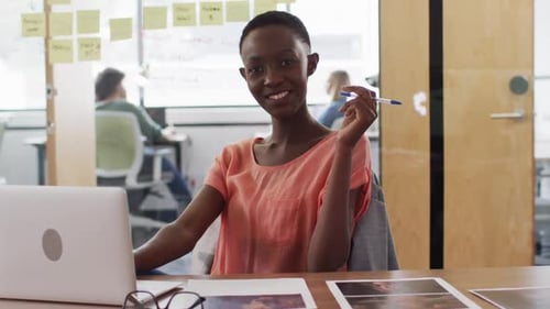 Portrait of african american businesswoman sitting at desk with laptop and smiling in office