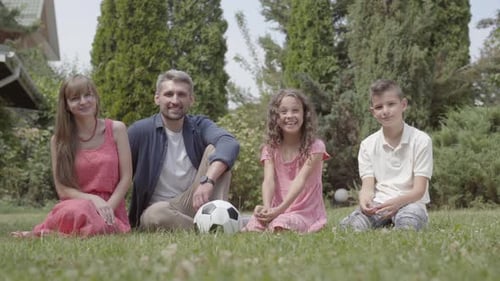 Happy Family Sitting on the Grass in the Garden Together. Mother, Father, Son, and Daughter