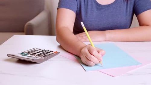 Woman is using a calculator to calculate her monthly expenses and write down her monthly accounting