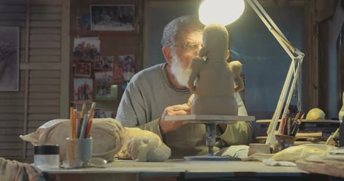 Old sculptor working on a clay sculpture in his small studio