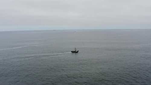 Drone aerial of a fishing vessel traveling alone into an open sea on a cloudy day.