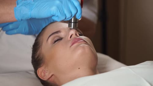 Assistentin bereitet das Gesicht einer Frau auf eine Mesotherapie-Behandlung ohne Injektion vor